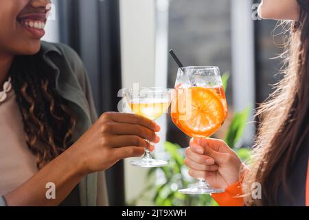 Beschnittene Ansicht von multiethnischen Freundinnen, die Cocktails im Café klirren, Stockbild Stockfoto