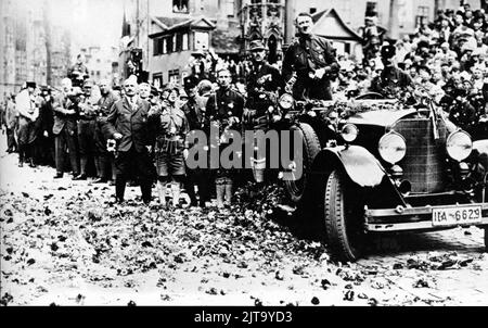 Ein Vintage-Foto um den 1 1929. August in Nürnberg, das den zukünftigen deutschen Nazi-Diktator Adolf Hitler zeigt, der in einem offenen Mercedes-Wagen posiert und während einer Party-Kundgebung Blumen wirft Stockfoto