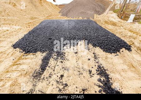 Die Maschine entleerte den heißen und frischen Asphalt in den Sand, in dem sich die Abdrücke der Räder befinden. Stockfoto