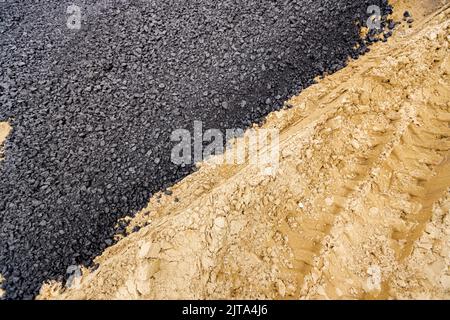 Die Maschine entleerte den heißen und frischen Asphalt in den Sand, in dem sich die Abdrücke der Räder befinden. Stockfoto