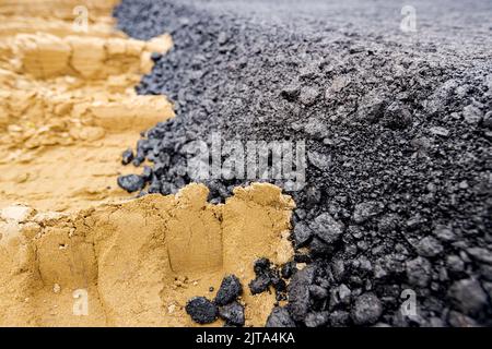 Die Maschine entleerte den heißen und frischen Asphalt in den Sand, in dem sich die Abdrücke der Räder befinden. Stockfoto