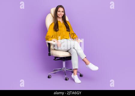 In voller Länge Foto von hr sitzen tragen Bluse Hose Schuhe auf lila Hintergrund isoliert Stockfoto