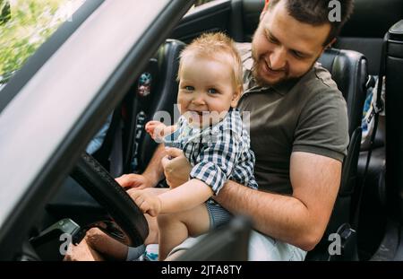 Papa zeigt seinem kleinen Sohn, wie er das Auto fährt, während er hinter dem Steuer sitzt Stockfoto