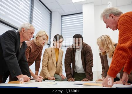 Gruppe von älteren Schülern, die während des Unterrichts am Tisch stehen und im Team mit ihrem Lehrer arbeiten Stockfoto