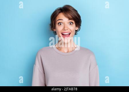 Portrait of adorable schöne nette Frau mit kurzen Frisur gekleidet grau Sweatshirt starrte offenen Mund isoliert auf blauem Hintergrund Stockfoto