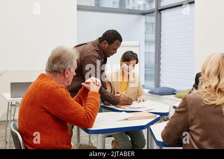 Afrikanischer Lehrer, der während des Unterrichts mit Schülern sprach, erklärte er ihnen neues Material, während sie an Schreibtischen im Klassenzimmer saßen Stockfoto