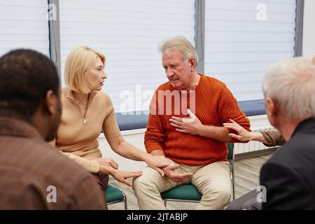 Deprimierter älterer Mann, der mit Menschen über sein Problem spricht, während sie in der psychologischen Klasse sitzen Stockfoto
