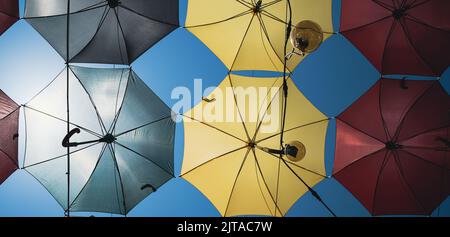 Vorderansicht Nahaufnahme Detail von bunten Regenschirmen und Edison Glühbirnen, die über einer Stadtstraße vor einem blauen Himmel hängen Stockfoto