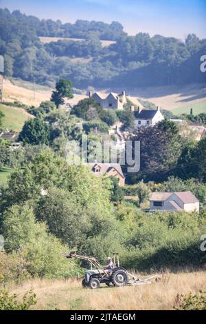 Ein Landwirt mäht in Coombe in der Nähe von Wotton-under-Edge, Gloucestershire, ein Feld zur Heuernte. Stockfoto