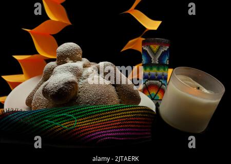 Brot verziert mit simulierten Kreuzknochen und Zucker auf einem Altar der Toten auf einem bunten Überlauf mit handgefertigten Papel picado und Lighte platziert Stockfoto