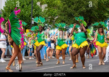 Notting Hill, London, Großbritannien. 29. August 2022. Europas größtes Straßenfest ist nach der Annullierung der Jahre aufgrund der Covid-Pandemie auf die Straßen von Notting Hill zurückgekehrt. Jamaikanische, exotische Tänzer und Musikgruppen zogen durch die Straßen, wobei Essen und Straßenunterhaltung in der Umgebung zur Veranstaltung hinzufügten. Die Grand Parade findet am Montag der Bankfeiertage statt, als Höhepunkt des dreitägigen Festivals, das 1966 begann. Gruppe tanzender Teilnehmer in hellen Kostümen Stockfoto