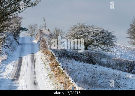 Eine verschneite Landstraße in der Nähe des Dorfes Tansley, Derbyshire, England Stockfoto