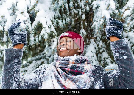 hispanischer Mann in rotem Hut mit Schneeflocke auf dem Gesicht, der Spaß hat und Weihnachtsstimmung im Park fühlt Stockfoto