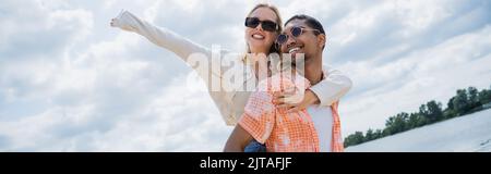 Junge afroamerikanische Mann Huckepack Freundin mit erhobener Hand, Banner Stockfoto