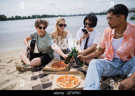 asiatische Frau, die Foto auf dem Smartphone in der Nähe von Freunden klirrende Bierflaschen Stockfoto