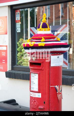 Skurrile bunte handgemachte gestrickte Wollmütze ziert eine traditionelle rote Säulenbox, die das Platin-Jubiläum von Königin Elizabeth II. Feiert England. Stockfoto