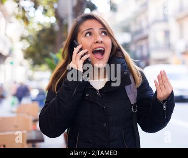 Wütende junge Latina, die draußen im Mobiltelefon schreit Stockfoto