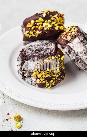 Schokoladenkekse-Eiscreme-Sandwiches mit dunkler Schokolade und Pistazien auf dem Teller, Draufsicht. Stockfoto