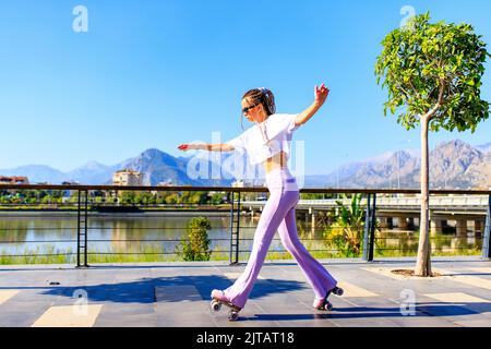 Glückliche Frau mit langen blonden Zöpfen Haare auf dem Rollschuh im Park Strand und Berg Hintergrund Stockfoto