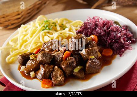 Von oben köstliches Rind- und Gemüsegulasch mit Spatzle-Pasta und Sauerkraut zum Abendessen auf dem Teller serviert Stockfoto