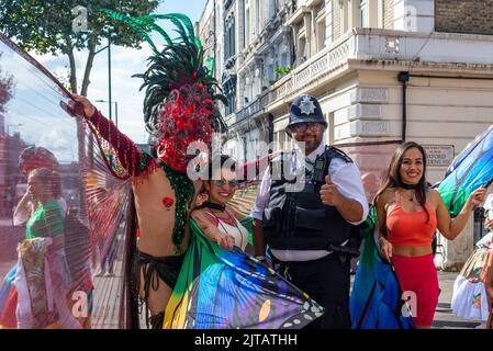 Notting Hill, London, Großbritannien. 29. August 2022. Europas größtes Straßenfest ist nach der Annullierung der Jahre aufgrund der Covid-Pandemie auf die Straßen von Notting Hill zurückgekehrt. Jamaikanische, exotische Tänzer und Musikgruppen zogen durch die Straßen, wobei Essen und Straßenunterhaltung in der Umgebung zur Veranstaltung hinzufügten. Die Grand Parade findet am Montag der Bankfeiertage statt, als Höhepunkt des dreitägigen Festivals, das 1966 begann. Polizist posiert mit Teilnehmern Stockfoto