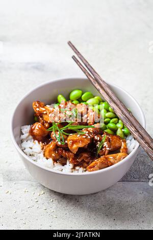 Teriyaki-Huhn mit Reis, Zwiebeln und Edamamabohnen in einer grauen Schüssel. Japanische Küche. Stockfoto