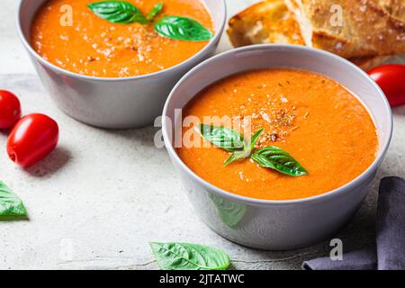 Traditionelle Gazpacho in grauer Schale. Sommertomatensuppe mit Basilikum. Veganes Lebensmittelkonzept. Stockfoto