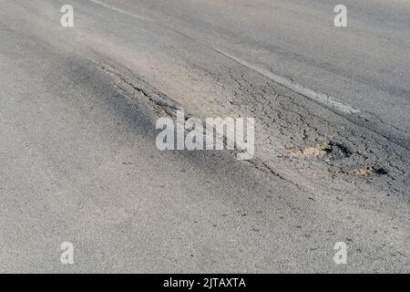 Deformierte Asphaltoberfläche mit Schlaglöchern, die durch schwere überlastete Lkw auf der Autobahn verursacht werden Stockfoto