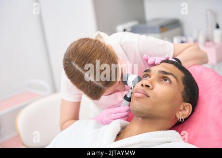 Professioneller Dermatologe, der eine Dermatoskopie bei einem männlichen Patienten durchführt Stockfoto