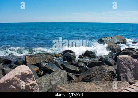 Wellen schlagen an einem sonnigen Tag mit blauem Himmel in Westerly, Rhode Island, in die felsige Küstenlinie ein -05 Stockfoto