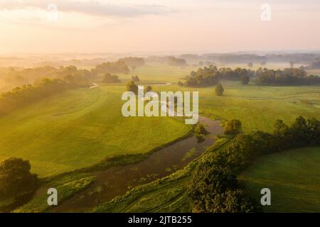 Die Natur ist landschaftlich reizvoll, der Fluss fließt durch ein grünes Land, das teilweise von Nebel bedeckt ist. Stockfoto