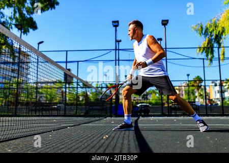 Reifer, hübscher Mann, der an sonnigen Tagen auf dem Tennisplatz Tennis spielt Stockfoto