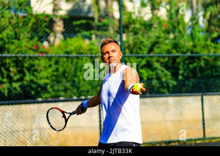 Älterer kaukasischer Mann, der auf dem Tennisplatz Tennis spielt und tagsüber im Freien an der frischen Luft Tennisschläger hält Stockfoto
