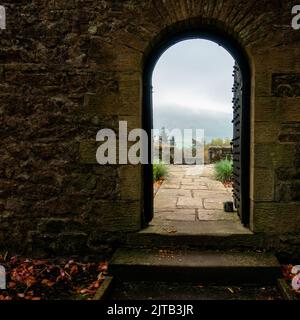 Blick auf die Gärten und nebligen Moore im Hintergrund durch einen Torbogen in der Parcevall Hall im Frühjahr, Yorkshire Dales National Park, Großbritannien Stockfoto