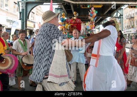 2 fröhliche Hindu-Männer tanzen unter dem erhöhten Zug A, um die Ratha Yatra Parade 2022 in Richmond Hill, Queens, NYC, zu feiern Stockfoto