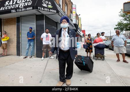 Eine Straßenszene auf der 101. Avenue mit einem Sikh-Reisenden im Vordergrund und anderen Männern und Frauen, die spazieren und abhängen. In Queens, NYC. Stockfoto