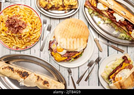 Set von Gerichten mit Wildgerichten, großer Hamburger mit Ei, gebratenem Speck und geschmolzenem Käse, Sandwich mit den gleichen Zutaten, Pommes mit Käse und Speck Stockfoto