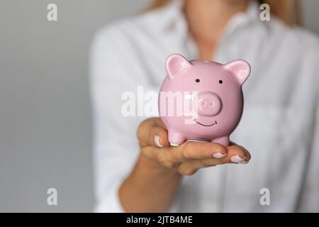 Weibliche Hände halten rosa Sparschwein in Innenräumen Anhäufung von Investitionen Krise Stockfoto