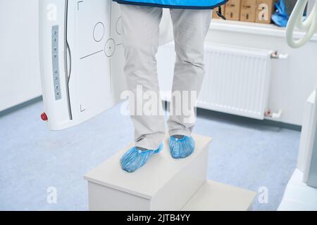 Beine in weißen Hosen und blauen Schuhüberzügen Stockfoto