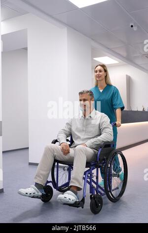 Der Arzt trägt einen Patienten im Rollstuhl Stockfoto