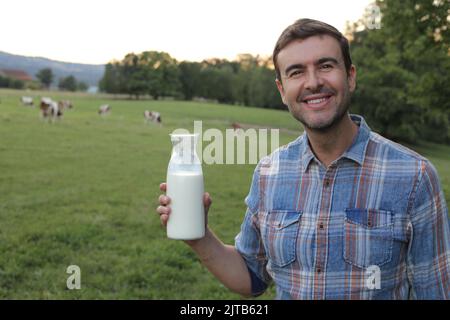 Bauer hält frische Milch mit Kühen im Hintergrund Stockfoto