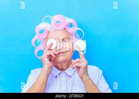 lady entfernt Make-up von ihrem Gesicht mit Wattepad und lächelt auf Kamera in blauen Studio-Hintergrund Stockfoto