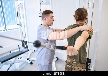 Iinstructor hilft Soldaten bei physiotherapeutischen Übungen im Rehabilitationszentrum Stockfoto