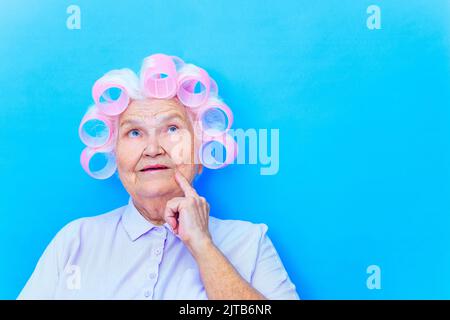 Charmante alte Frau mit Lockenwicklern auf weiß grauen Haaren tragen Hemd immer bereit für Datum isoliert auf hellblauen Hintergrund Stockfoto