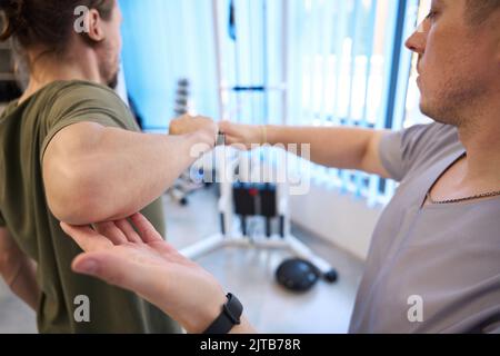 Der Kursleiter unterstützt den Patienten bei der Durchführung von Übungen am Power Simulator Stockfoto