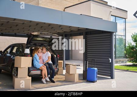 Fröhliche Eltern umarmen ihre Tochter und sehen sie im Auto sitzen Stockfoto