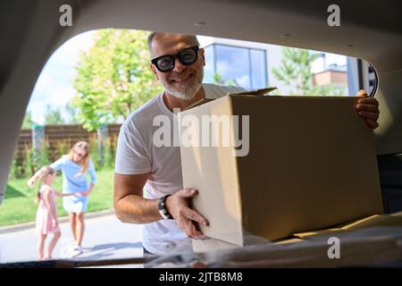 Der Mann nimmt den Kasten aus dem Kofferraum. Blick von innen Auto Stockfoto