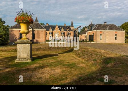 Schloss Twickel nahe Ambt Delden, Gemeinde Hof van Twente, Niederlande, erhebt sich hinter einer goldenen Blumenurne mit roten Blüten im Vordergrund neben dem Wassergraben. Das Schloss, das erstmals 1347 erwähnt wurde, ist von einem Gut mit mehr als 4.000 Hektar und über 150 Bauernhöfen umgeben. Stockfoto