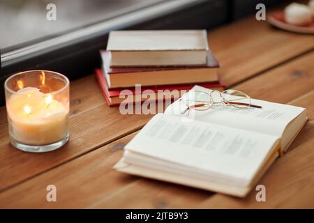 Bücher, Gläser und Kerzen brennen auf der Fensterbank Stockfoto