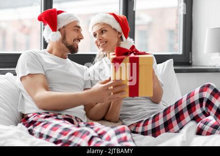 Glückliches Paar mit weihnachtsgeschenk im Bett zu Hause Stockfoto